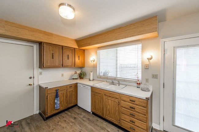 Kitchen with light countertops, wood finished floors, a sink, white dishwasher, and brown cabinetry | Image 12