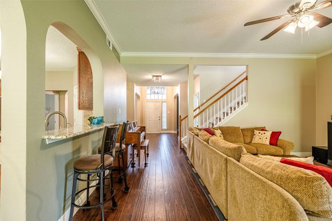 Living area with arched walkways, crown molding, a textured ceiling, a ceiling fan, and dark wood finished floors | Image 14