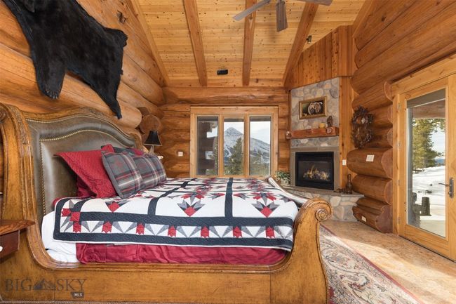 Main level primary bedroom with detailed ceiling, stone fireplace, log walls and access to outside hot tub patio | Image 16
