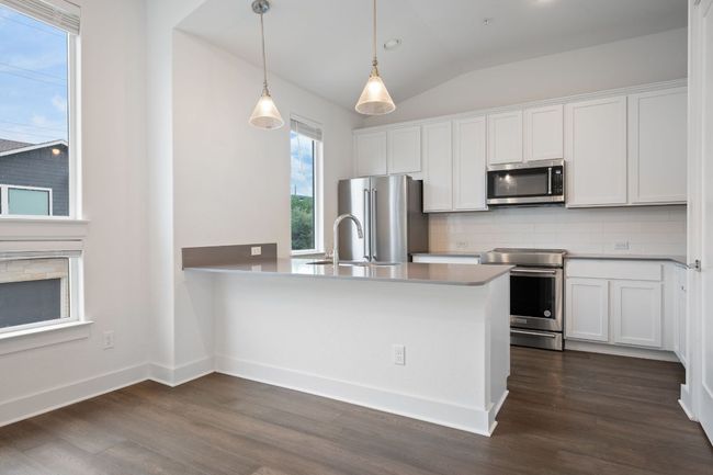 Kitchen featuring appliances with stainless steel finishes, tasteful backsplash, white cabinets, dark wood finished floors, and decorative light fixtures | Image 10