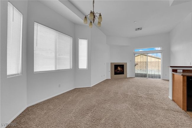 Unfurnished living room with a chandelier, a tile fireplace, carpet, baseboards, and visible vents | Image 4