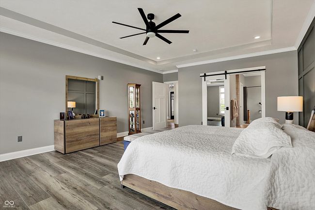 bedroom featuring a barn door, wood finished floors, a raised ceiling, baseboards, and recessed lighting | Image 25