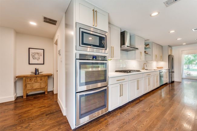Kitchen featuring appliances with stainless steel finishes, wall chimney range hood, dark wood-style flooring, a sink, and light countertops | Image 17