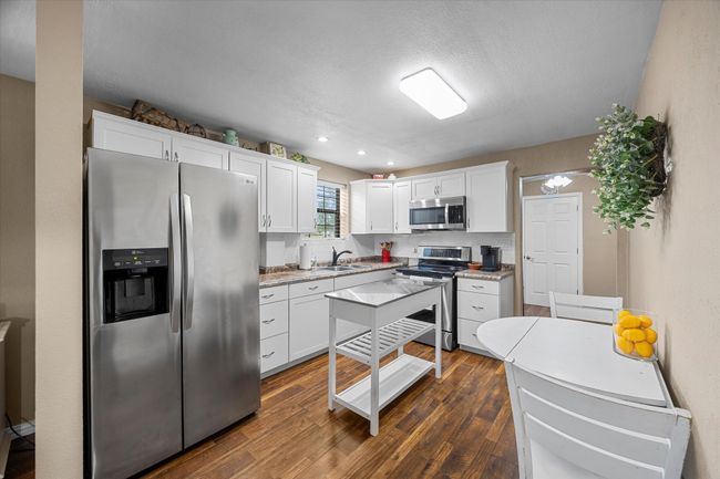 Kitchen with stainless steel appliances, dark wood-style flooring, white cabinets, light countertops, and recessed lighting | Image 13