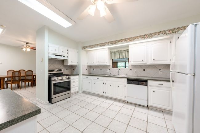 Kitchen featuring white appliances, ceiling fan, dark countertops, under cabinet range hood, and decorative backsplash | Image 17