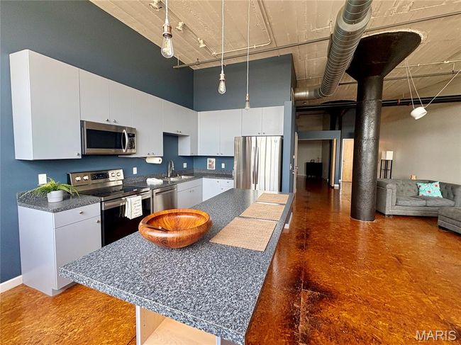 Kitchen featuring appliances with stainless steel finishes, a towering ceiling, white cabinetry, dark countertops, and decorative light fixtures | Image 12