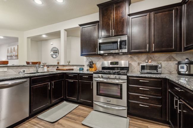 Kitchen with appliances with stainless steel finishes, a sink, stone countertops, light wood finished floors, and decorative backsplash | Image 9