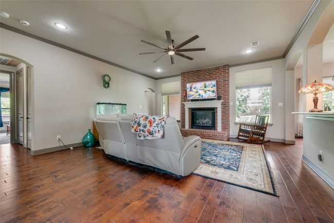 Living area with a ceiling fan, plenty of natural light, crown molding, arched walkways, and a brick fireplace | Image 12