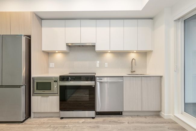 Kitchen with stainless steel appliances, a sink, modern cabinets, light countertops, and light wood-style flooring | Image 8