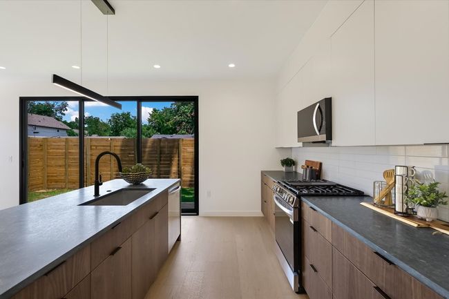 Kitchen with modern cabinets, appliances with stainless steel finishes, light wood finished floors, dark countertops, and decorative backsplash | Image 11