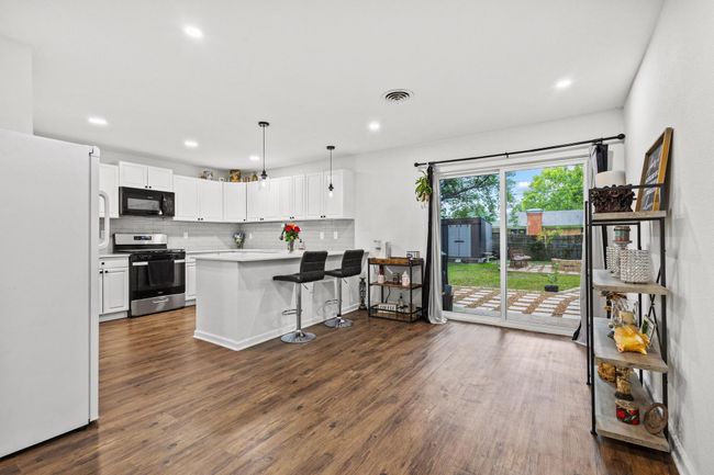 Kitchen featuring black microwave, freestanding refrigerator, stainless steel gas range, backsplash, and dark wood-style floors | Image 6