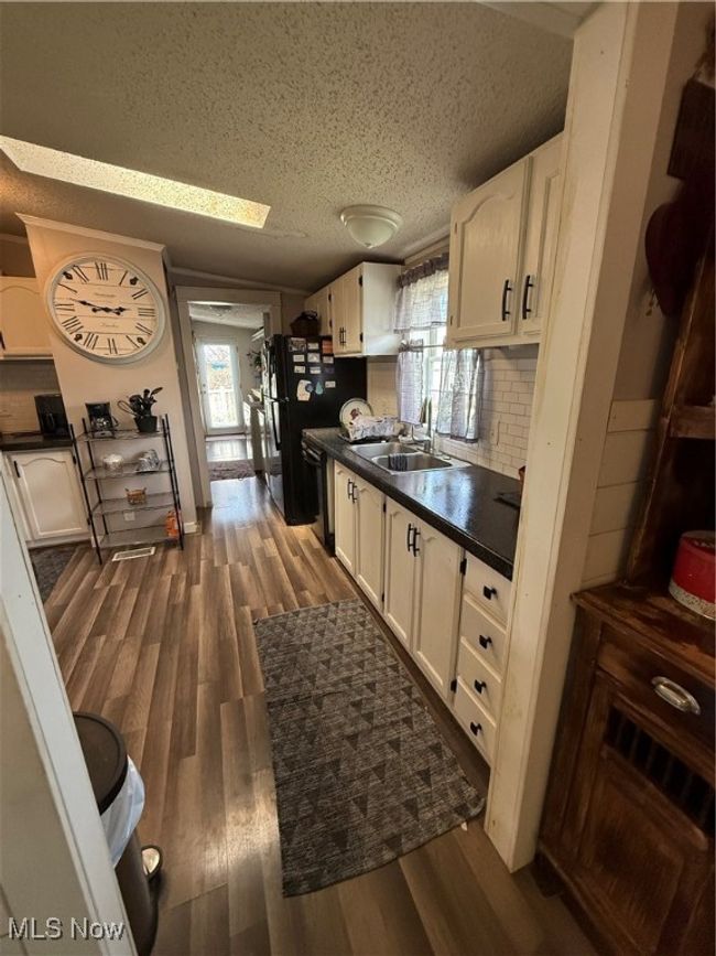 Kitchen featuring dark countertops, a sink, dark wood-type flooring, a textured ceiling, and white cabinetry | Image 10
