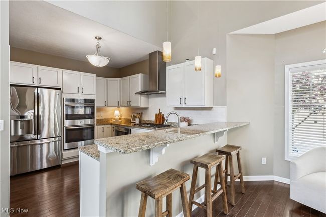 Kitchen featuring bar seating, granite countertops, white cabinetry, and stainless steel appliances | Image 11