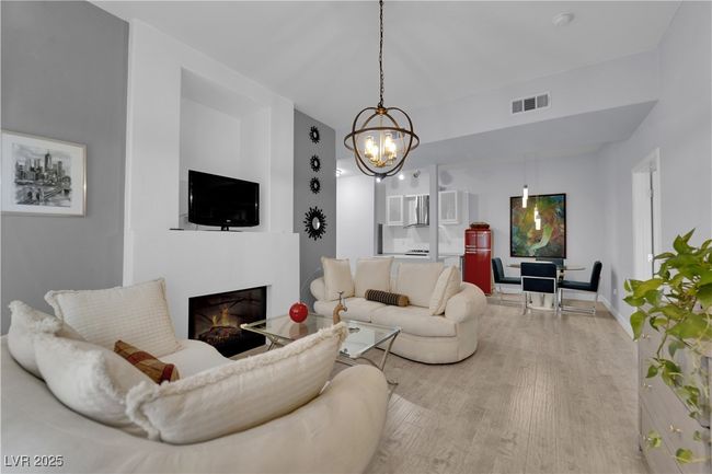 Living area with wood finished floors, a lit fireplace, and a chandelier | Image 10
