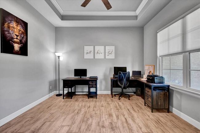 Office space with a tray ceiling, wood finished floors, ornamental molding, baseboards, and a ceiling fan | Image 11