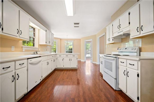 Kitchen featuring white appliances, a peninsula, dark wood-type flooring, white cabinetry, and under cabinet range hood | Image 7