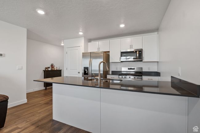 Kitchen with dark countertops, a sink, dark wood-type flooring, and appliances with stainless steel finishes | Image 5