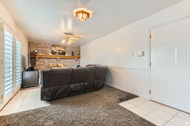 Living room featuring light tile patterned flooring, ceiling fan, light colored carpet, and brick wall | Image 8