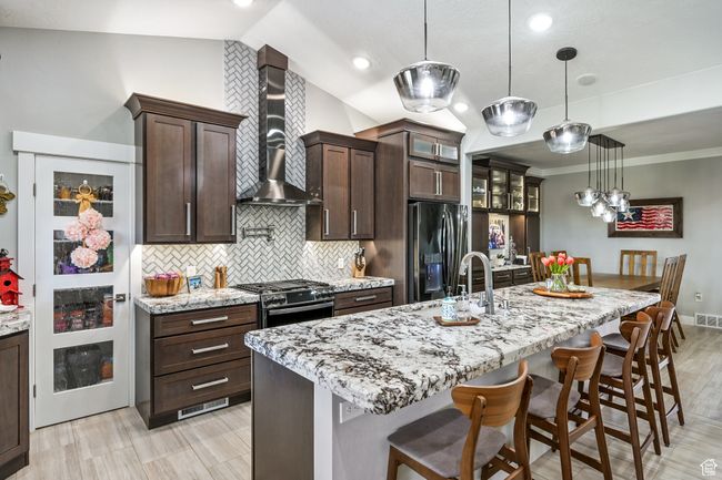Kitchen with appliances with stainless steel finishes, wall chimney exhaust hood, backsplash, a kitchen bar, and dark brown cabinets | Image 24
