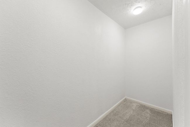 This photo shows a small, well-lit, carpeted room with white textured walls, suitable for use as a storage space or compact office. | Image 24