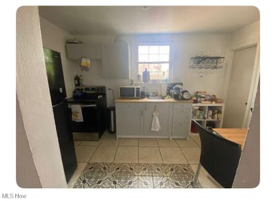 Kitchen with black electric range, white cabinets, and light tile patterned floors | Image 2