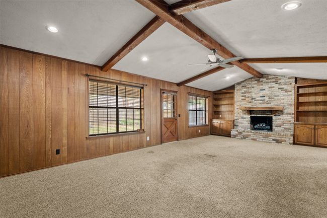 Unfurnished living room with wood walls, carpet, ceiling fan, a brick fireplace, and vaulted ceiling with beams | Image 8