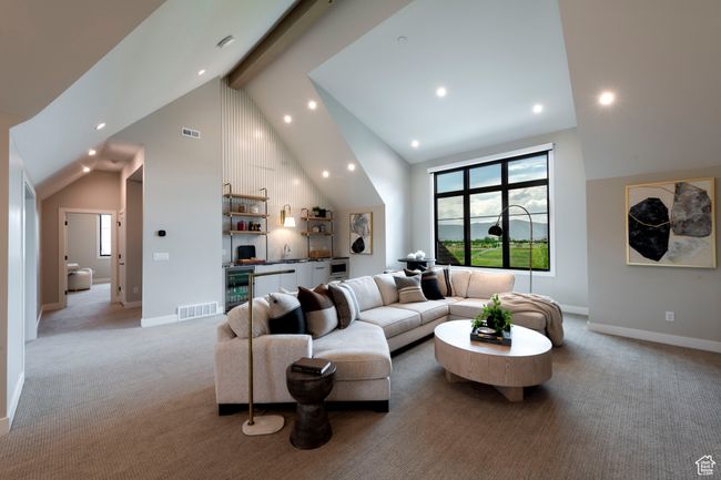 Living area featuring wine cooler, bar with sink, high vaulted ceiling, light carpet, and beamed ceiling | Image 43