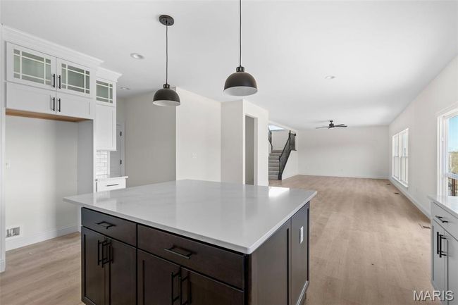 Kitchen with light wood finished floors, white cabinetry, a ceiling fan, hanging light fixtures, and glass insert cabinets | Image 15