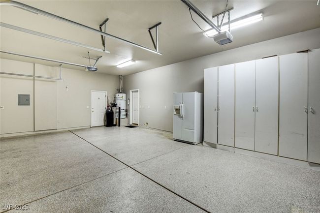 Garage featuring white refrigerator with ice dispenser, secured water heater, electric panel, and a garage door opener | Image 43