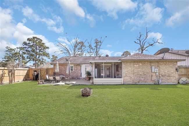 This backyard features a spacious, grassy area with a brick exterior house. There's a cozy patio with outdoor seating, perfect for relaxing or entertaining. A wooden fence provides privacy, and mature trees add a natural touch. | Image 26