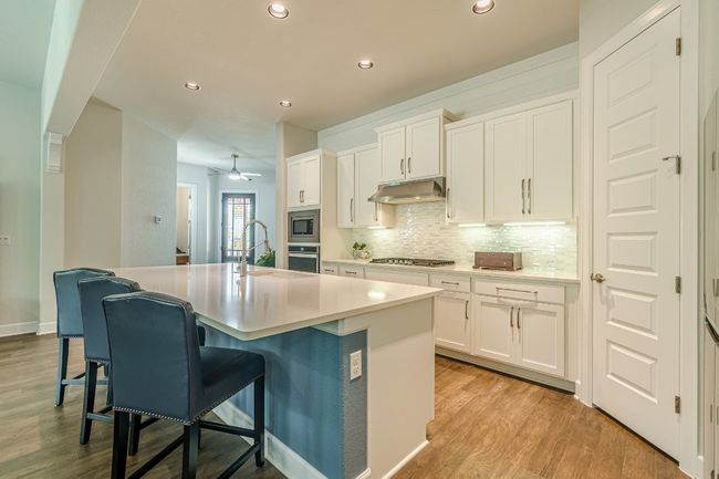 Kitchen featuring stainless steel appliances, under cabinet range hood, light wood finished floors, tasteful backsplash, and a sink | Image 15