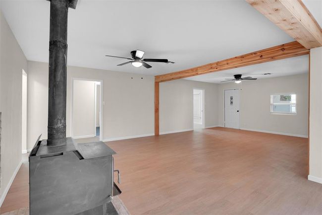 Living room featuring beamed ceiling, light wood-type flooring, ceiling fan, and a wood stove | Image 15