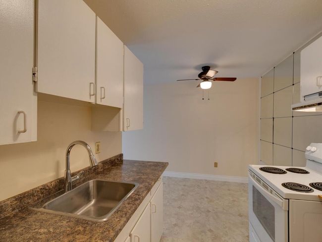Kitchen with white electric stove, dark countertops, ceiling fan, and a sink | Image 14