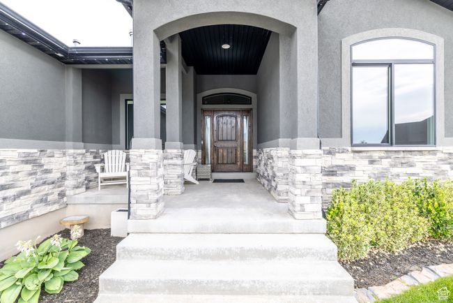Doorway to property with stucco siding, stone siding, and a porch | Image 7