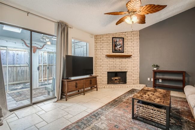 Living room with ceiling fan, a textured ceiling, vaulted ceiling, a fireplace, and stone tile flooring | Image 4