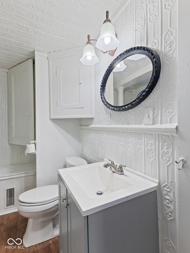 half bath with toilet, wallpapered walls, vanity, wood finished floors, and visible vents | Image 22