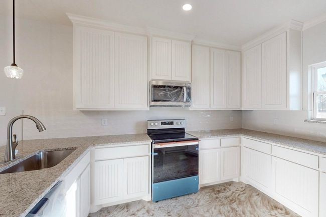 Kitchen featuring stainless steel appliances, white cabinets, a sink, and light stone counters | Image 14
