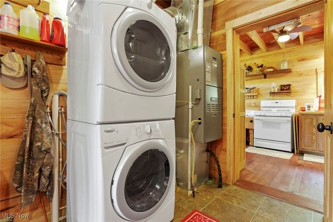 Clothes washing area featuring wooden walls, stacked washing machine and dryer, and a ceiling fan | Image 11