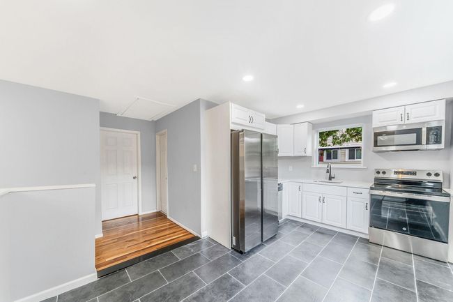 Kitchen featuring white cabinetry, light countertops, stainless steel appliances, dark tile patterned flooring, and a sink | Image 6