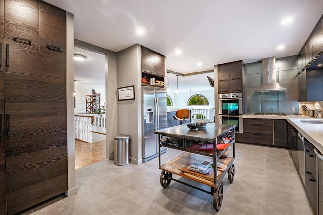 Kitchen featuring appliances with stainless steel finishes, wall chimney exhaust hood, light tile patterned flooring, tasteful backsplash, and light countertops | Image 13