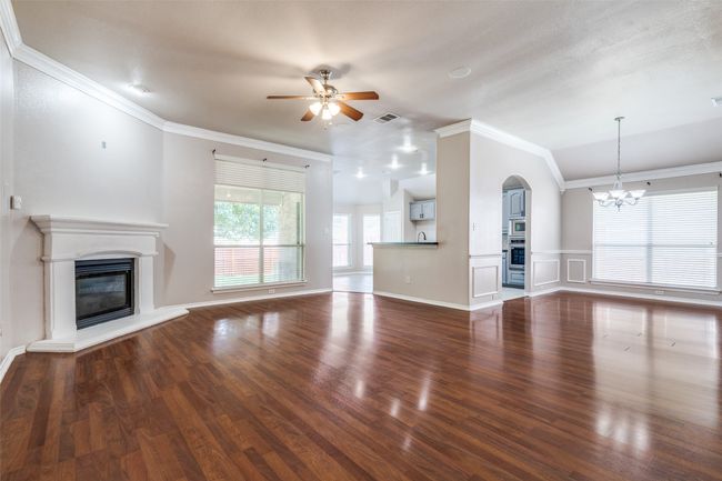 Unfurnished living room featuring a glass covered fireplace, a ceiling fan, a chandelier, wood finished floors, and lofted ceiling | Image 5