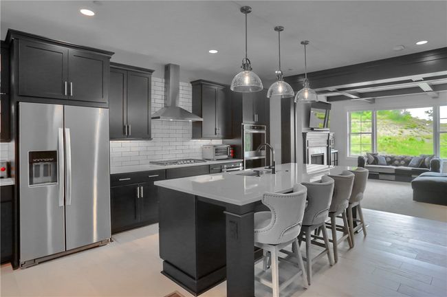 This modern, contemporary home features wide-plank hardwood flooring throughout, sleek black cabinetry, a 9x5 quartz island, and designer lighting that perfectly complements the open-concept layout and coffered ceiling in the light-filled family room. | Image 7
