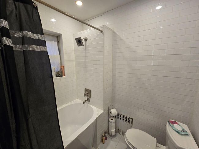 Bathroom featuring recessed lighting, toilet, radiator heating unit, shower / bath combo with shower curtain, and tile walls | Image 10