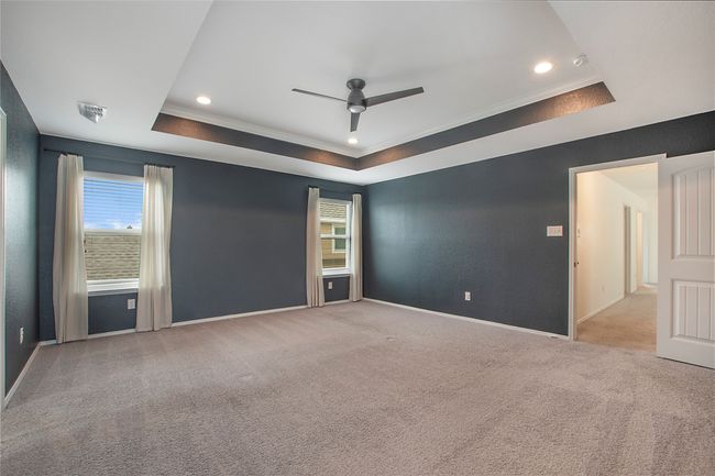 Carpeted spare room featuring a raised ceiling, plenty of natural light, a ceiling fan, ornamental molding, and recessed lighting | Image 21