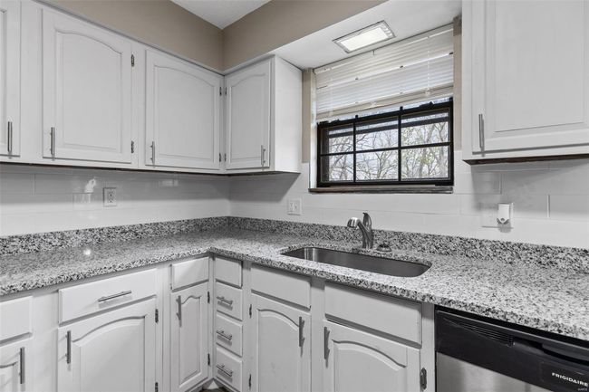Kitchen featuring tasteful backsplash, stainless steel dishwasher, a sink, light stone counters, and white cabinets | Image 10