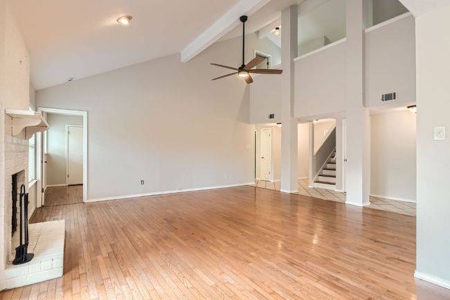 Unfurnished living room featuring ceiling fan, light wood finished floors, a brick fireplace, high vaulted ceiling, and visible vents | Image 6