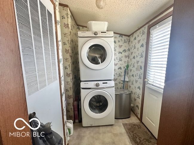 washroom featuring stacked washer / drying machine, wallpapered walls, plenty of natural light, and a heating unit | Image 10