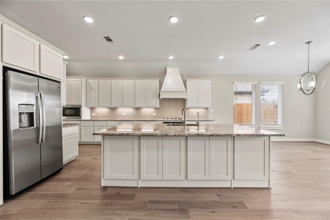 Ditch the takeout and enjoy home-cooked meals more often in this gorgeous kitchen, featuring a sprawling island with a deep basin sink, granite countertops, a custom hood vent, stainless steel appliances, and a stylish herringbone tile backsplash. Abundant cabinetry and warm under-cabinet lighting complete the space. Every detail thoughtfully designed to inspire your inner chef. | Image 17