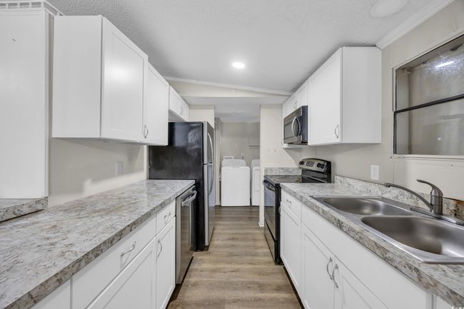 Kitchen featuring appliances with stainless steel finishes, washing machine and dryer, a sink, light wood-style floors, and white cabinetry | Image 9