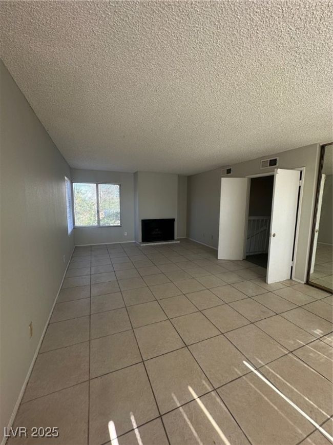 Unfurnished living room featuring a textured ceiling, a fireplace, light tile patterned floors, and baseboards | Image 16